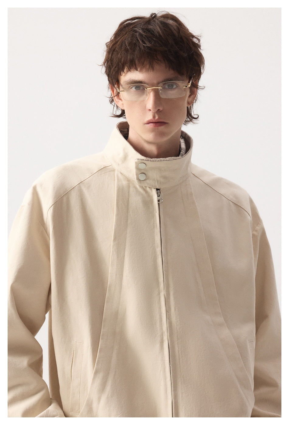 Front view of a model in a pale beige zip jacket with a high collar, snap buttons and side pockets.