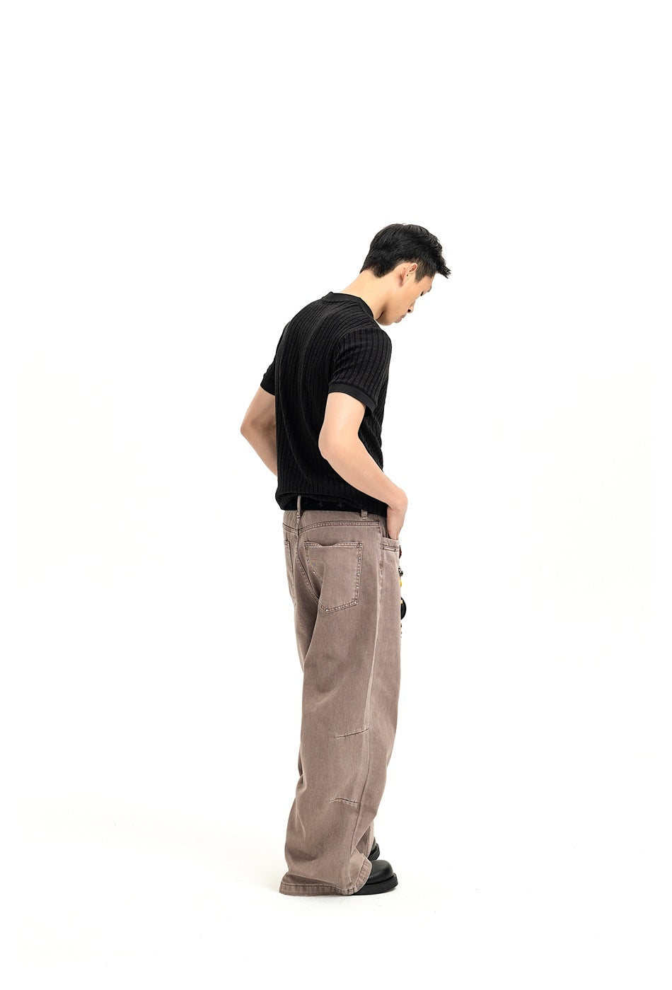 Side and rear view of a man wearing a black ribbed short-sleeve shirt and taupe wide-leg trousers.