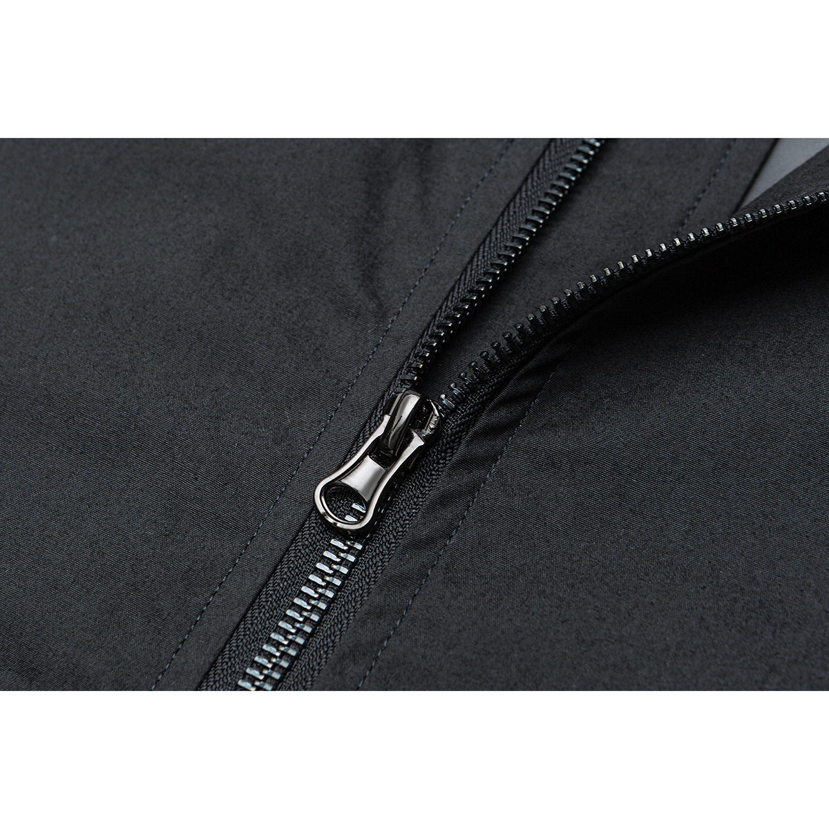 Close-up of the dark jacket's shiny metal zipper pull and teeth against the fabric.