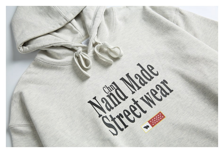 Close-up of a light gray hoodie showing its drawstrings and black “Hand Made Street wear” chest print.