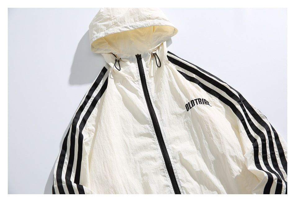 Front view of an ivory hooded jacket with a black zipper, black sleeve stripes, drawcords, and chest lettering.