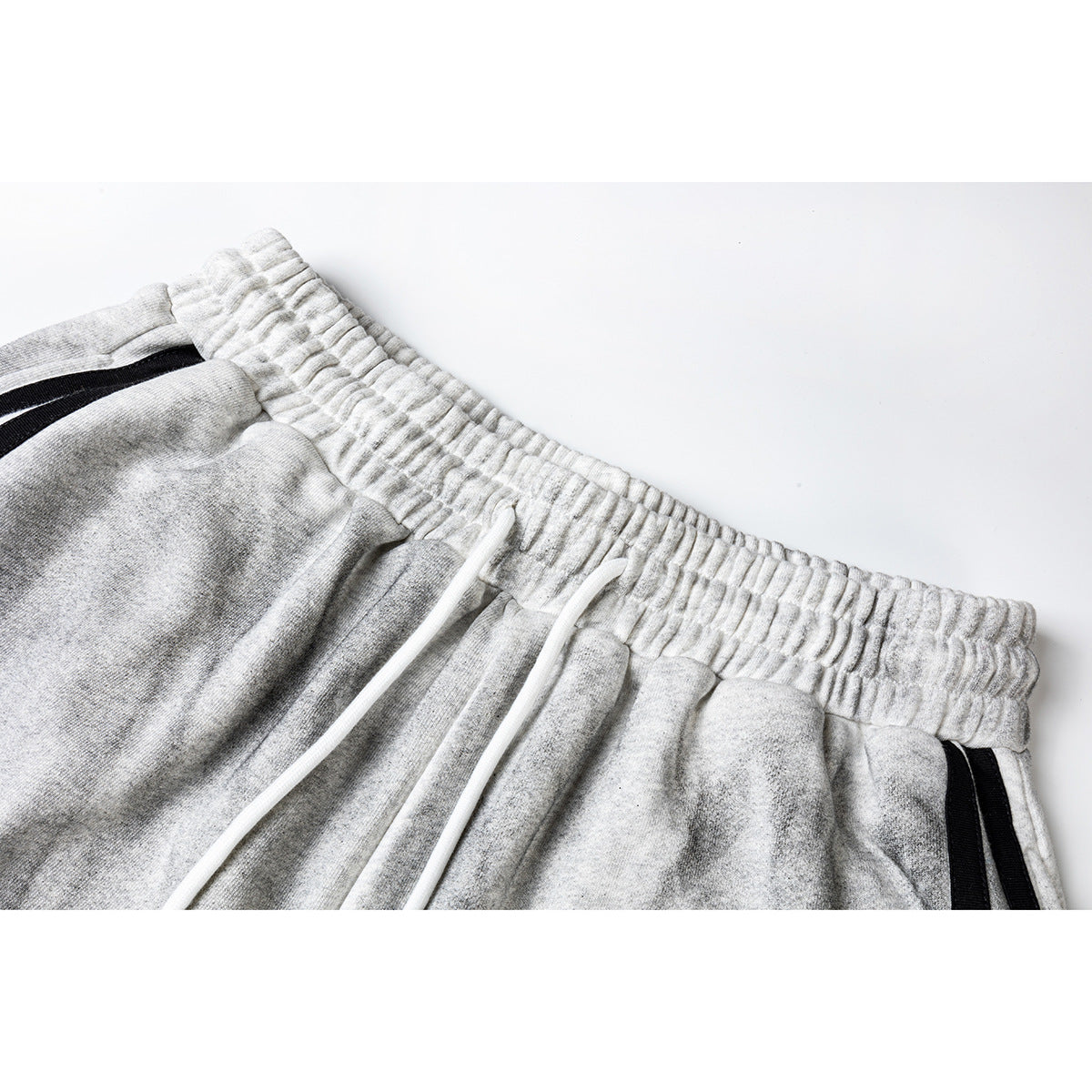 Close-up of gray athletic shorts showing the elastic waistband, white drawstrings, and black side stripes.