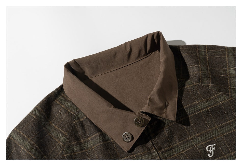 Close-up of a brown collar with two dark buttons on a dark plaid garment and a small white embroidered mark.