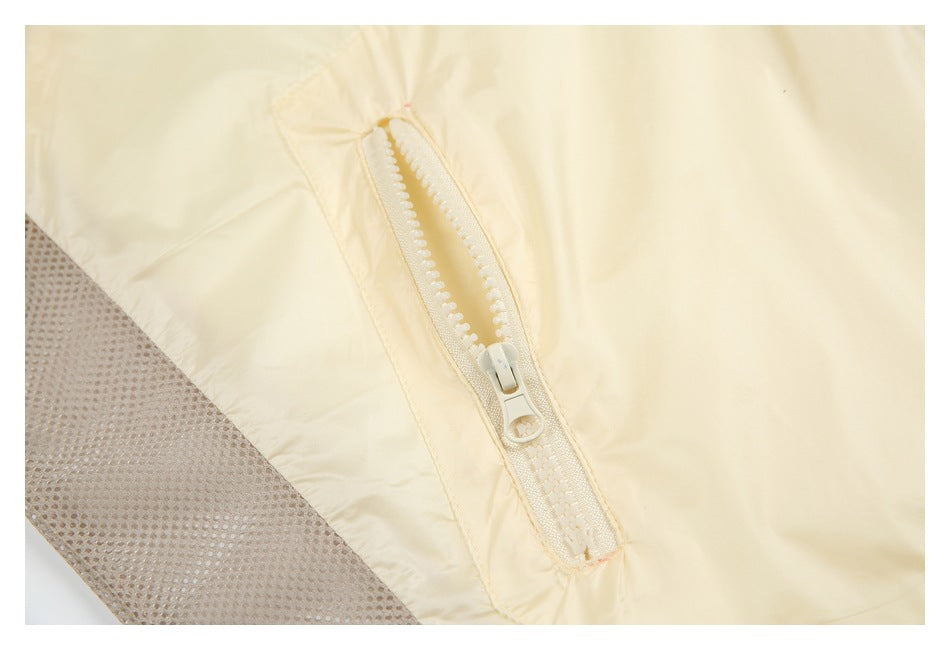 Close-up of a zip pocket on a pale cream jacket, beside a taupe mesh panel.