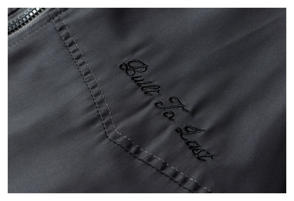 Close-up of black embroidered lettering and stitching on dark charcoal fabric.
