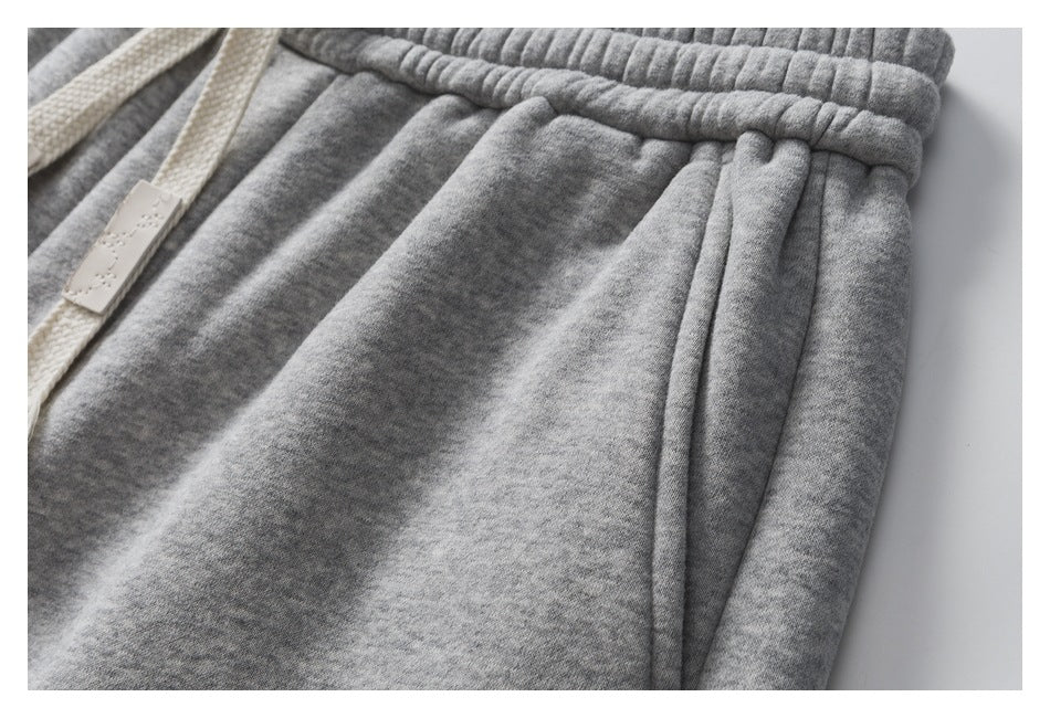 Close-up of gray sweatpants showing the front pocket opening and cream drawstring detail.
