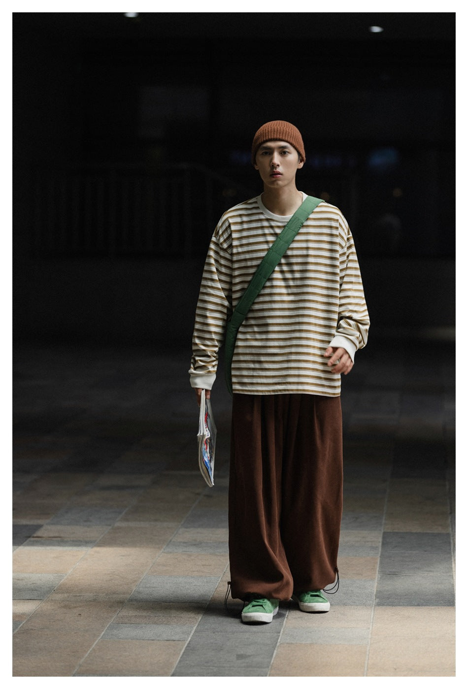 Full-length view of a model wearing brown wide-leg trousers, a striped long-sleeve shirt, and a rust beanie.