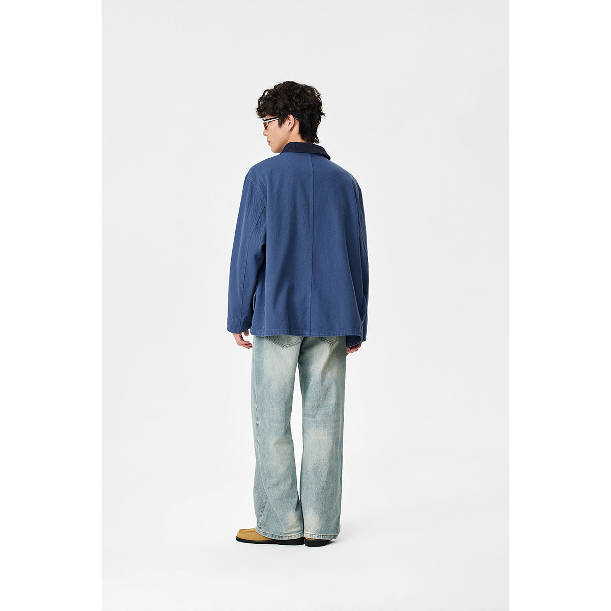 Rear view of a model wearing a blue work jacket with a plain back and dark collar.