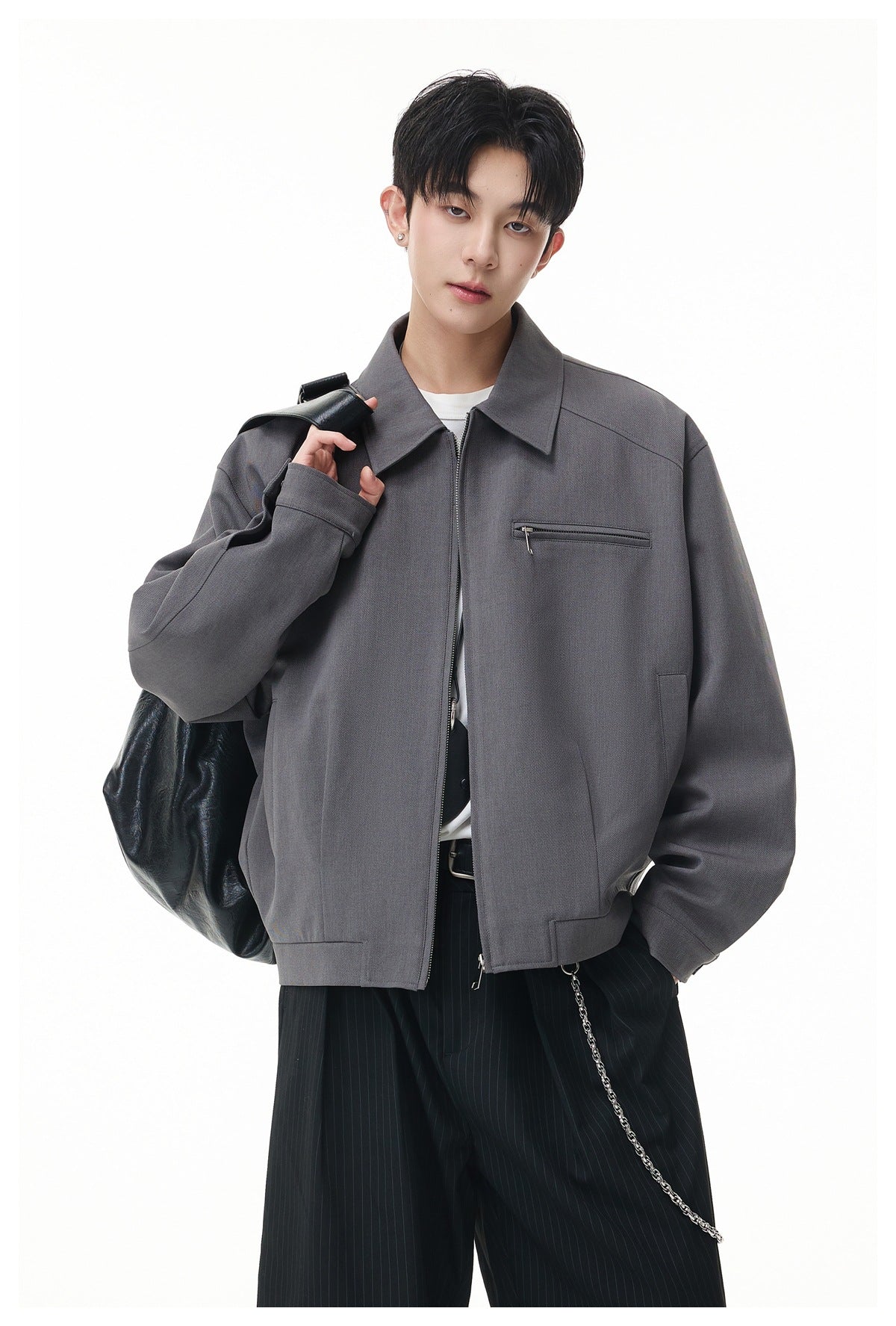 Close-up of model in gray collared zip jacket with chest zip pocket, black bag and pinstripe pants with chain