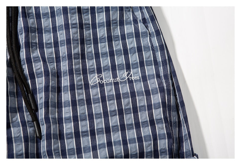 Close-up of blue and gray plaid pants showing white embroidered lettering beside the black drawstring.