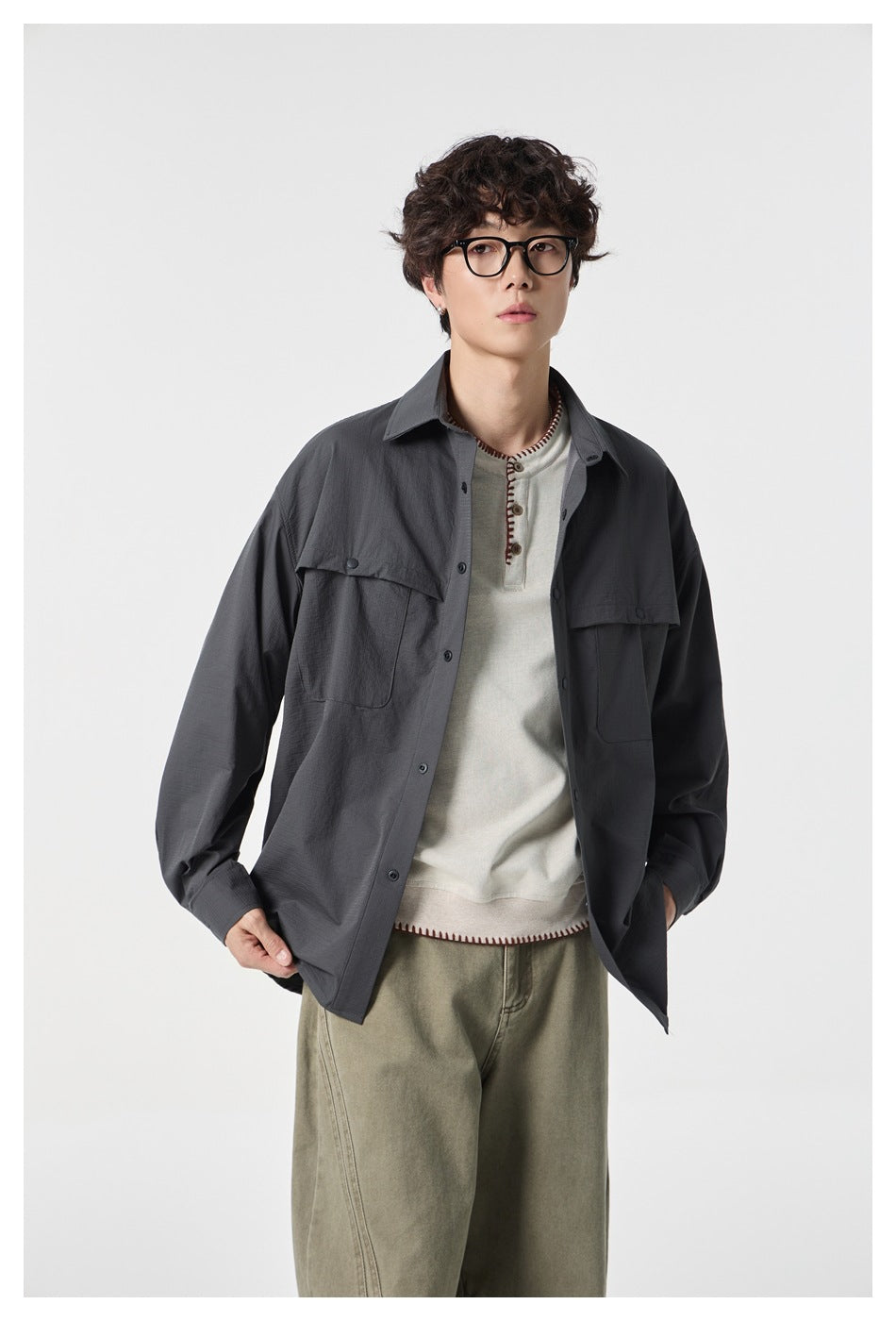 Model wearing an open charcoal oversized button-up shirt with flap chest pockets over a cream top.