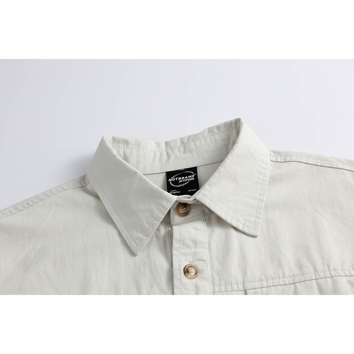 Close-up of an off-white button-up shirt collar, front buttons, and sewn-in neck label.