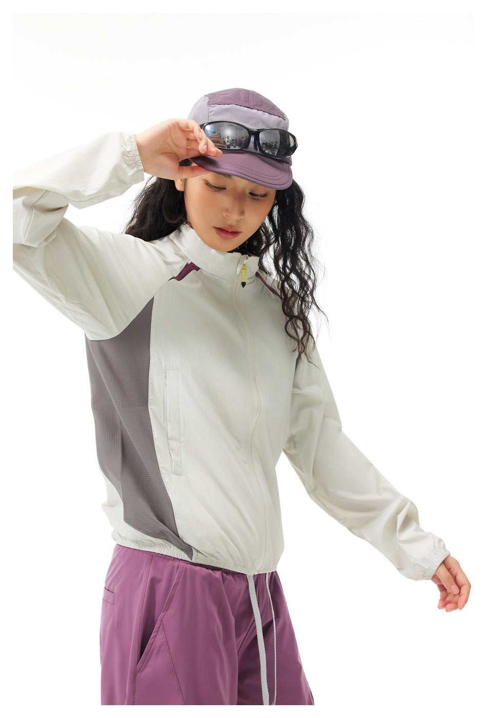 Angled view of a model wearing an off-white zip jacket with gray side panels and plum pants.