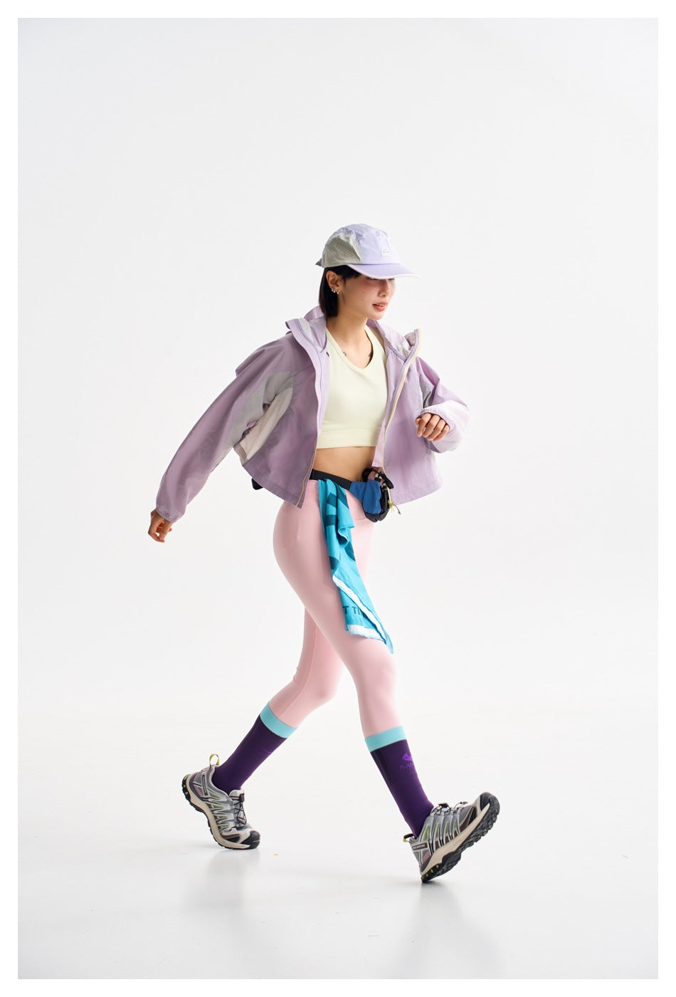 Model walking in a cropped lavender jacket, pale yellow crop top, and light pink leggings.