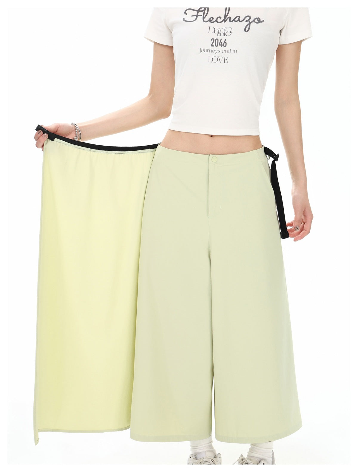 Close view of a model opening the pale yellow-green wrap skirt to show its wide-leg trouser construction and black trim.
