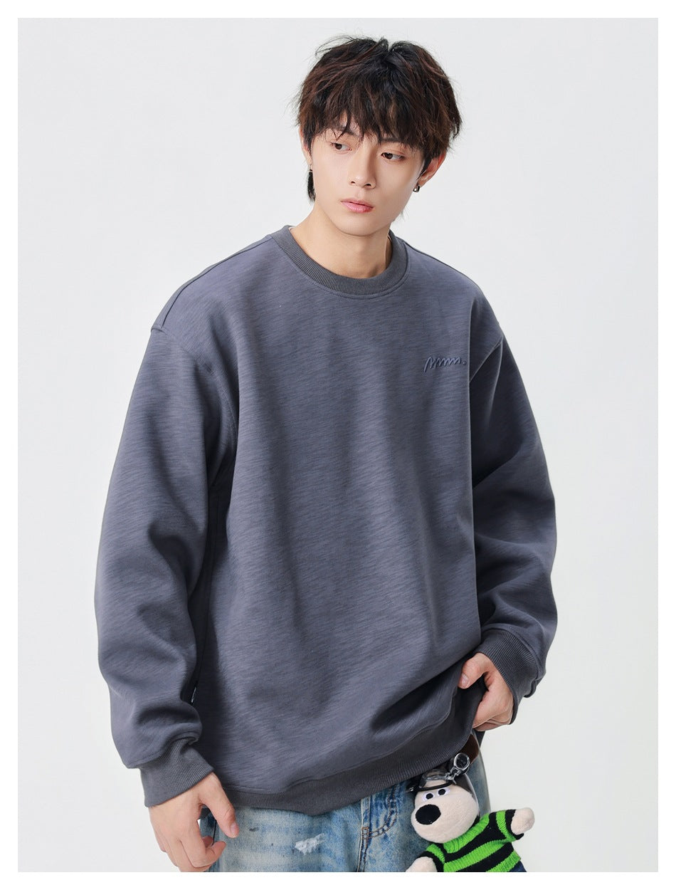 Model in a charcoal gray oversized crewneck sweatshirt with a small embroidered chest mark and ribbed hem and cuffs.