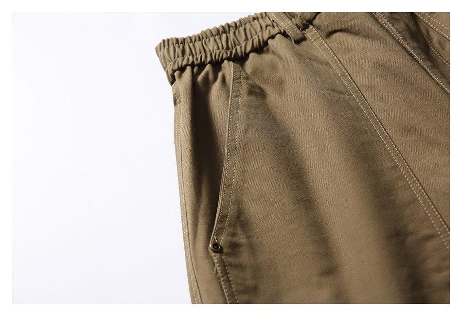 Close-up of khaki trousers showing an elastic waistband, stitched seams and a small snap fastener.