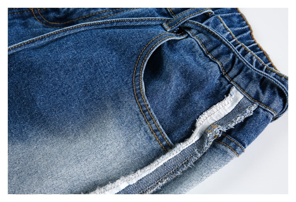 Inside view of blue jeans showing a front pocket opening, waistband, and overlocked seam.