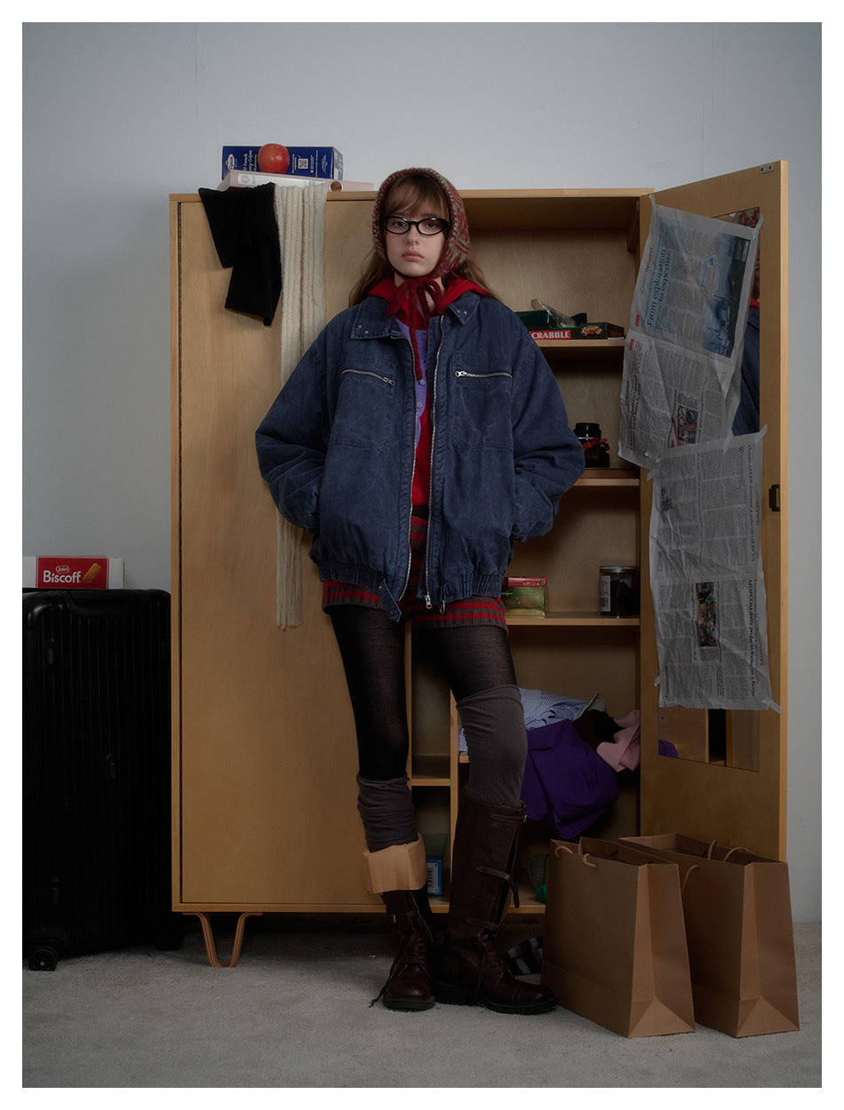 Model wearing a navy washed zip jacket over a red top with a patterned head scarf, standing by a wooden cabinet