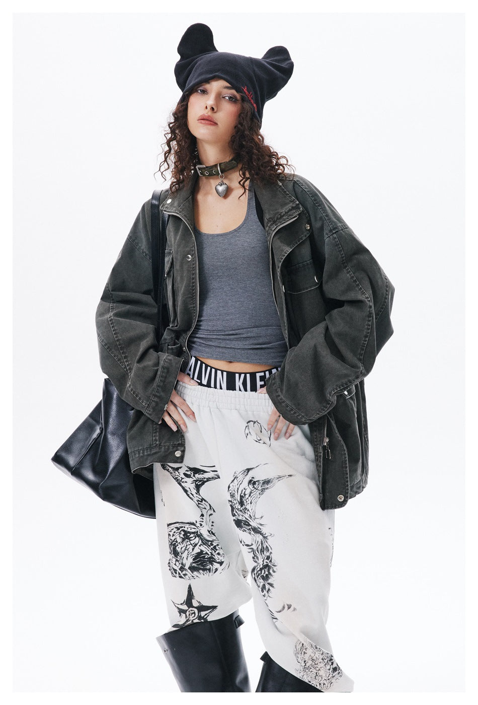 Model wearing an open charcoal jacket over a gray top and white graphic pants with black boots.