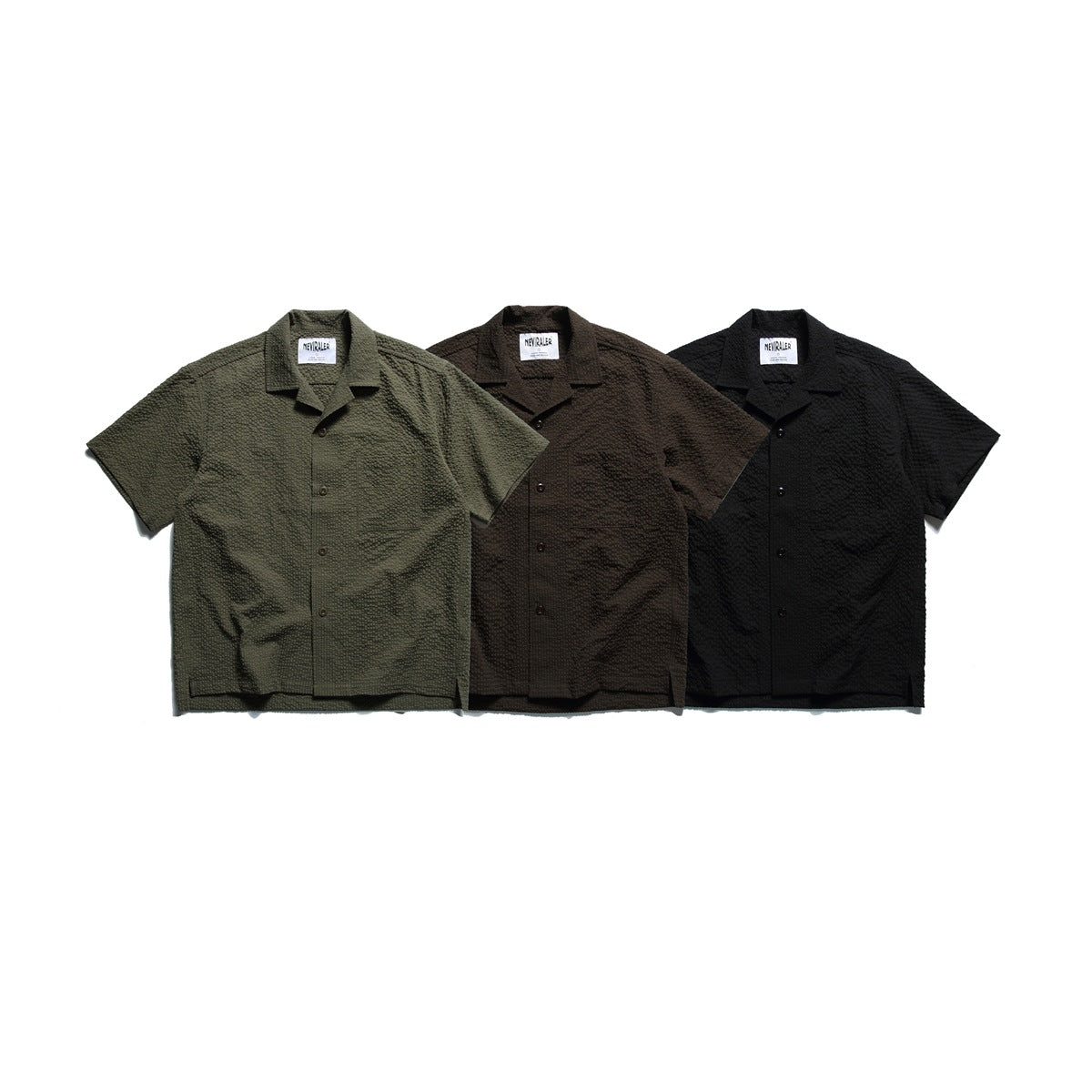 Three short-sleeve button-up shirts with chest pockets shown from the front in olive, dark brown, and black.