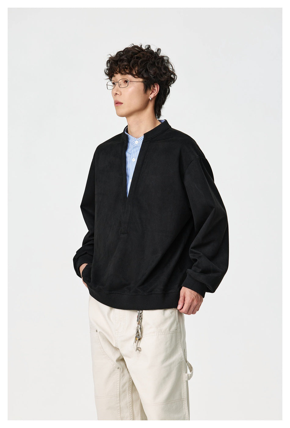 Three-quarter side view of a model in a black oversized split-neck pullover and cream trousers.