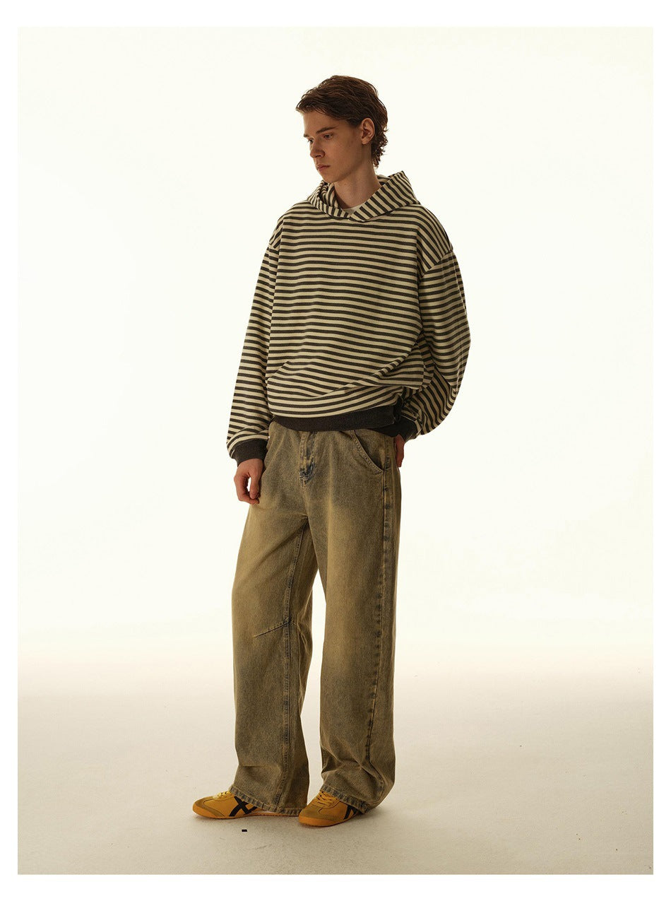 Model in a tan and dark striped hoodie and loose olive trousers, shown standing at a three-quarter angle.