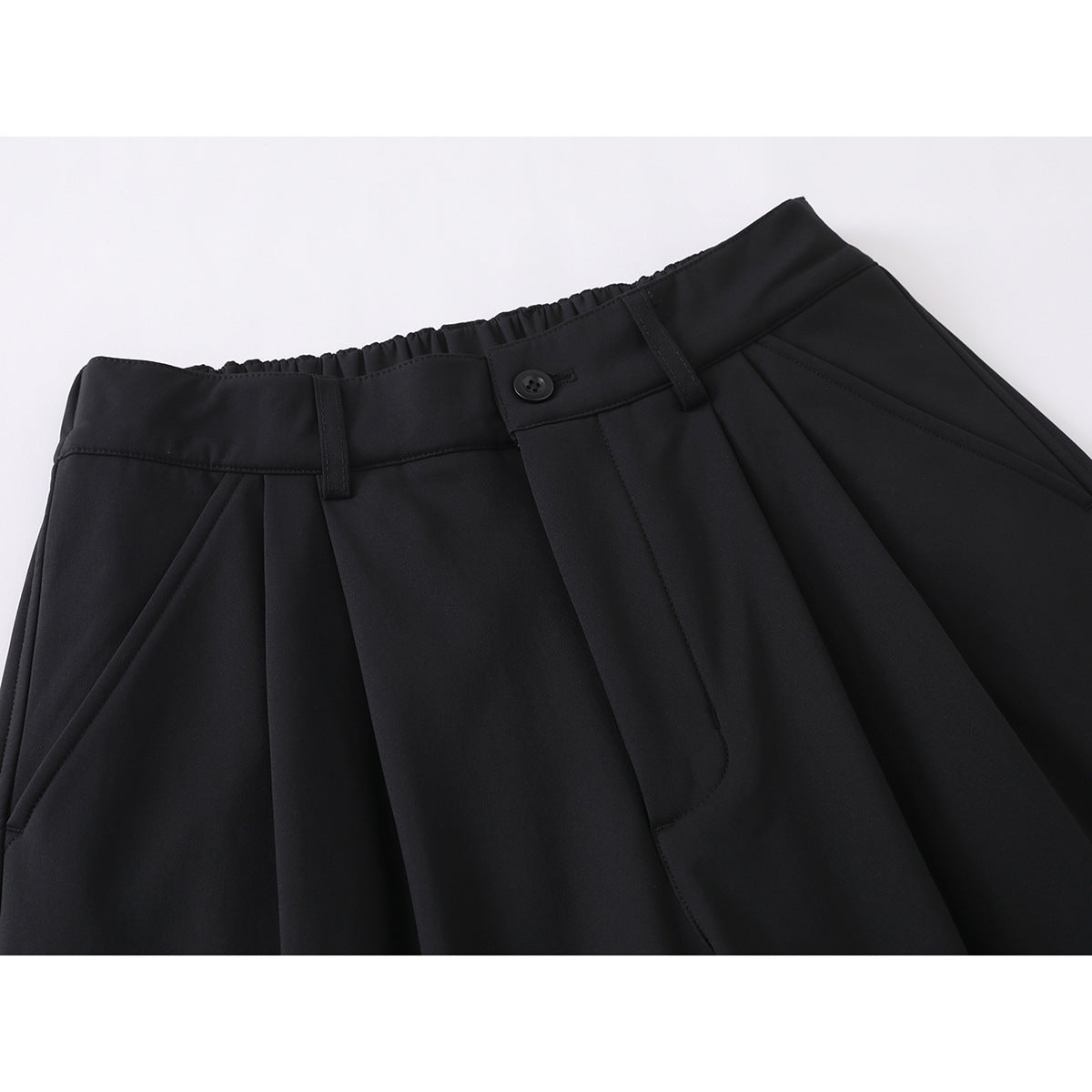 Close-up of black trousers showing the waistband, button, belt loops, pleats, and angled front pocket.