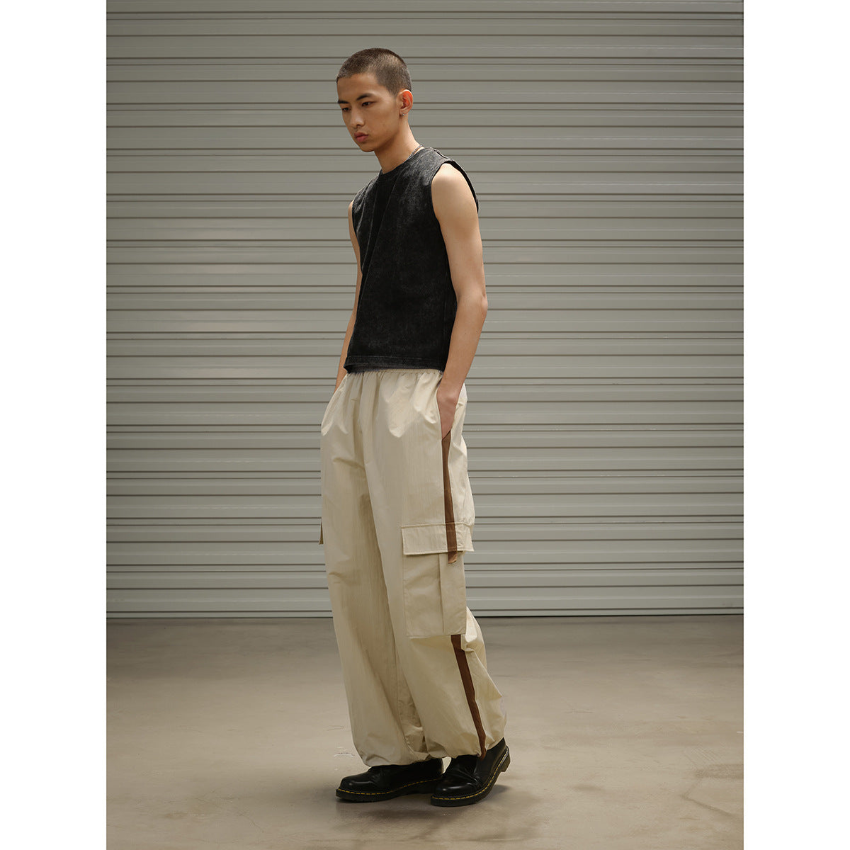 Three-quarter side view of a model wearing a black sleeveless top and loose beige cargo pants with side pockets.