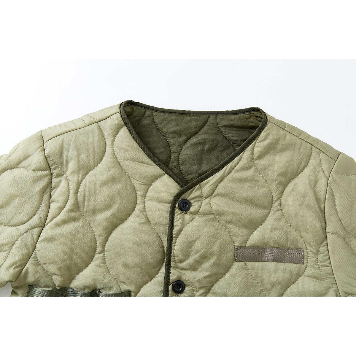 Close-up of a light olive quilted jacket front with dark binding, black buttons and a narrow chest tab.