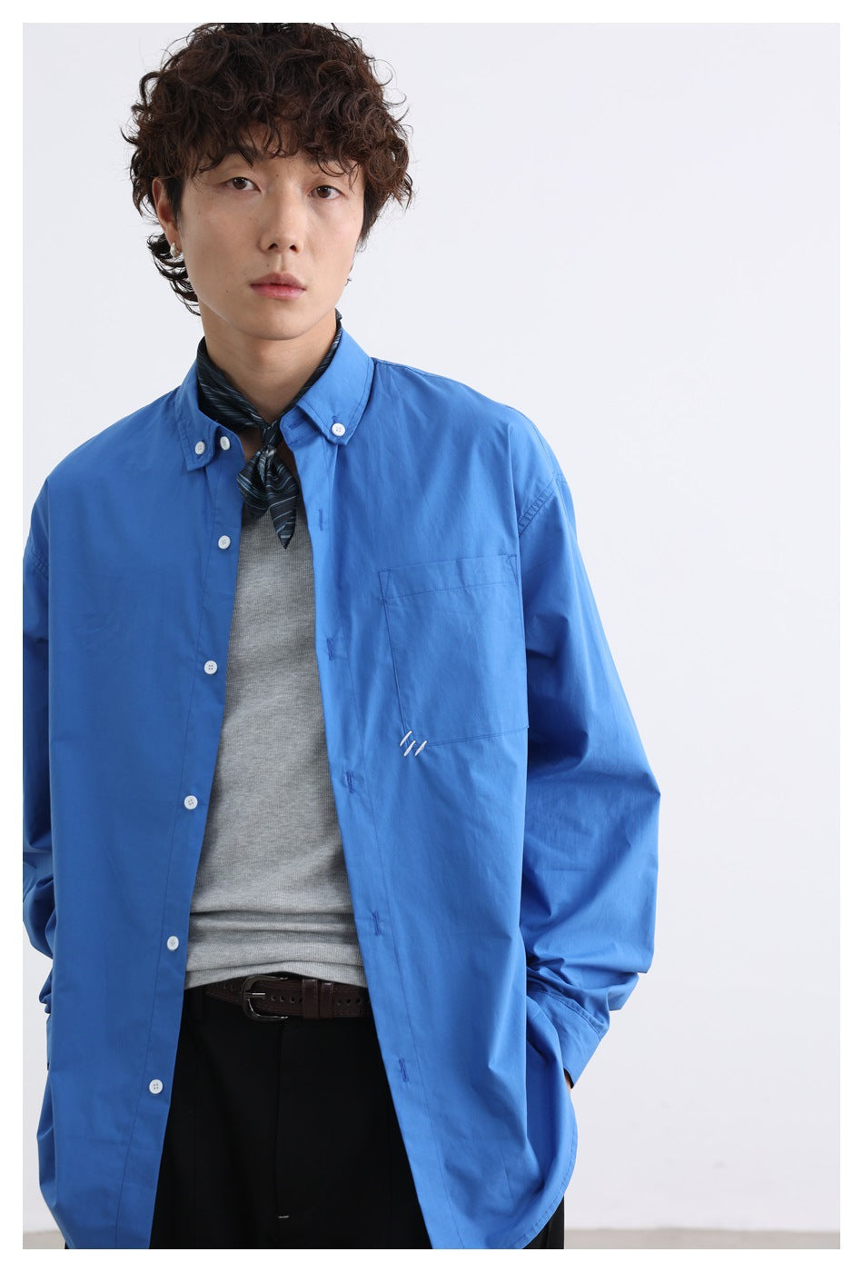 Model wearing an open blue button-down shirt over a gray tank, with a patterned neck scarf and black pants