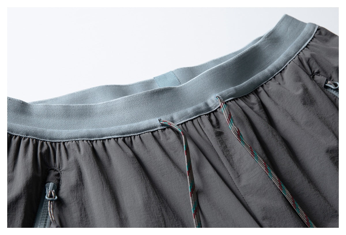 Close-up of charcoal shorts with a pale blue-gray elastic waistband, multicolored drawcords, and zip pockets.
