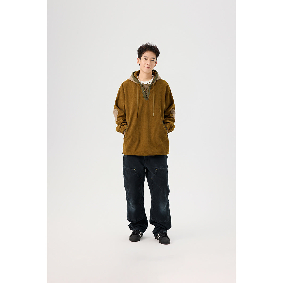 Full-length front view of a model wearing a mustard-brown hooded pullover with a lace-up neckline and black wide-leg pants.