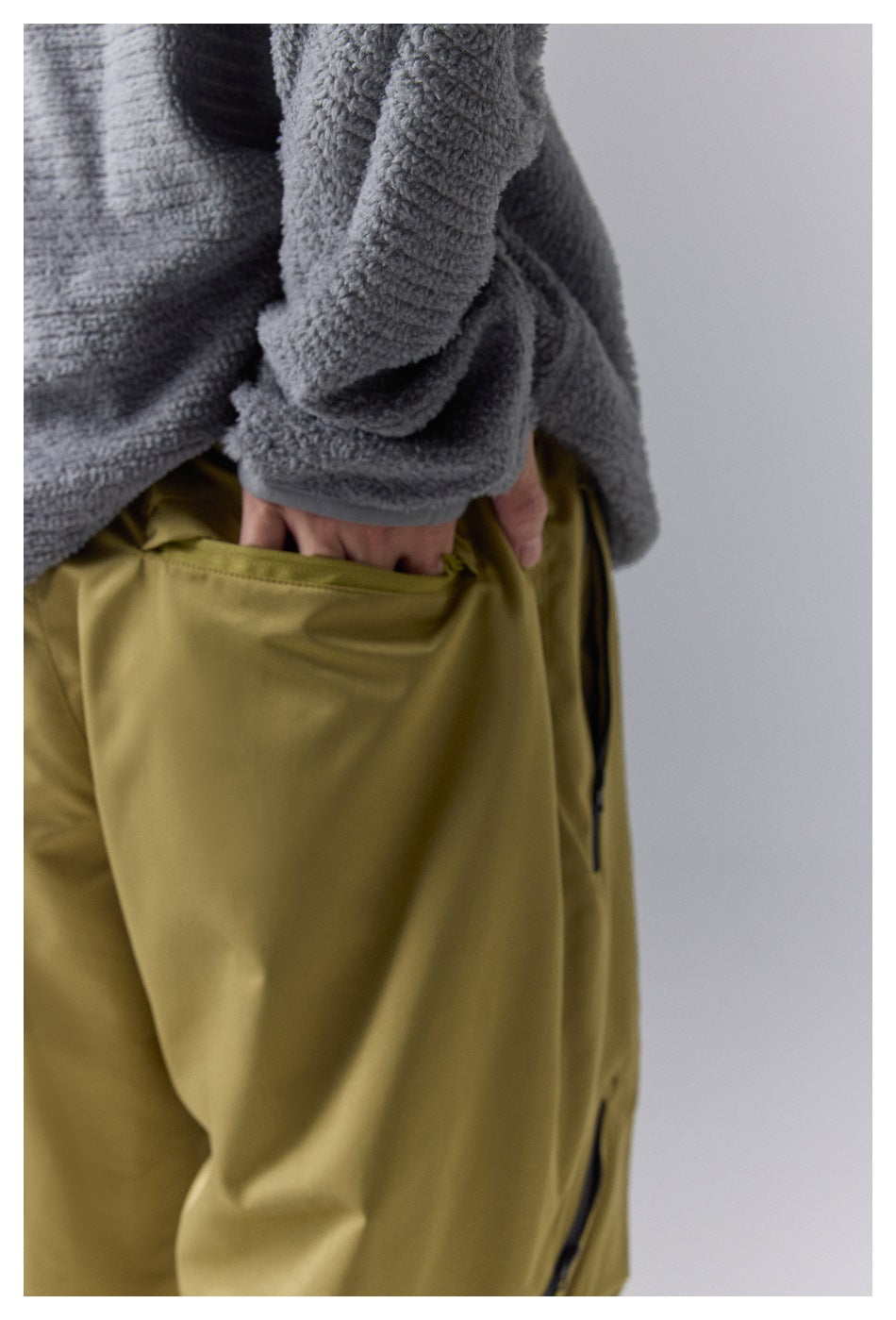 Close-up of a hand reaching into the large pocket of olive-yellow pants.