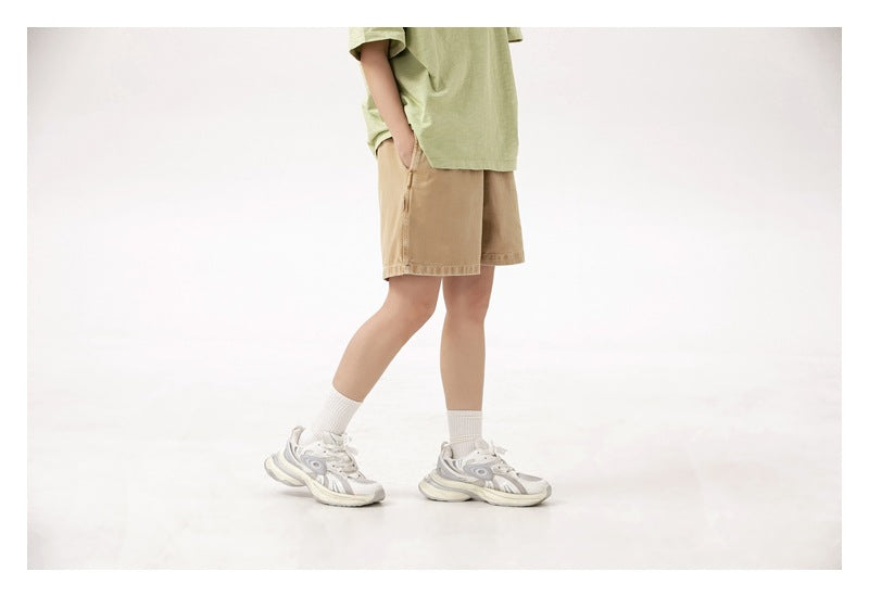 Cropped side-front view of a person wearing tan shorts and a pale green T-shirt.