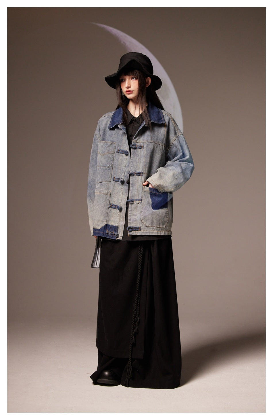 Full-length front view of a model wearing a gray and dark blue denim jacket over a long black outfit.