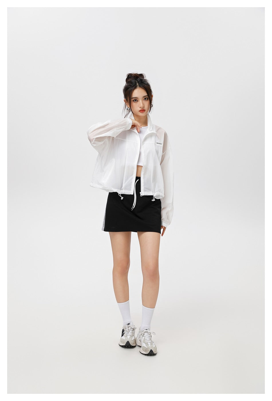 Model wearing a white zip-front jacket with a stand collar and drawstring hem over a black skirt.