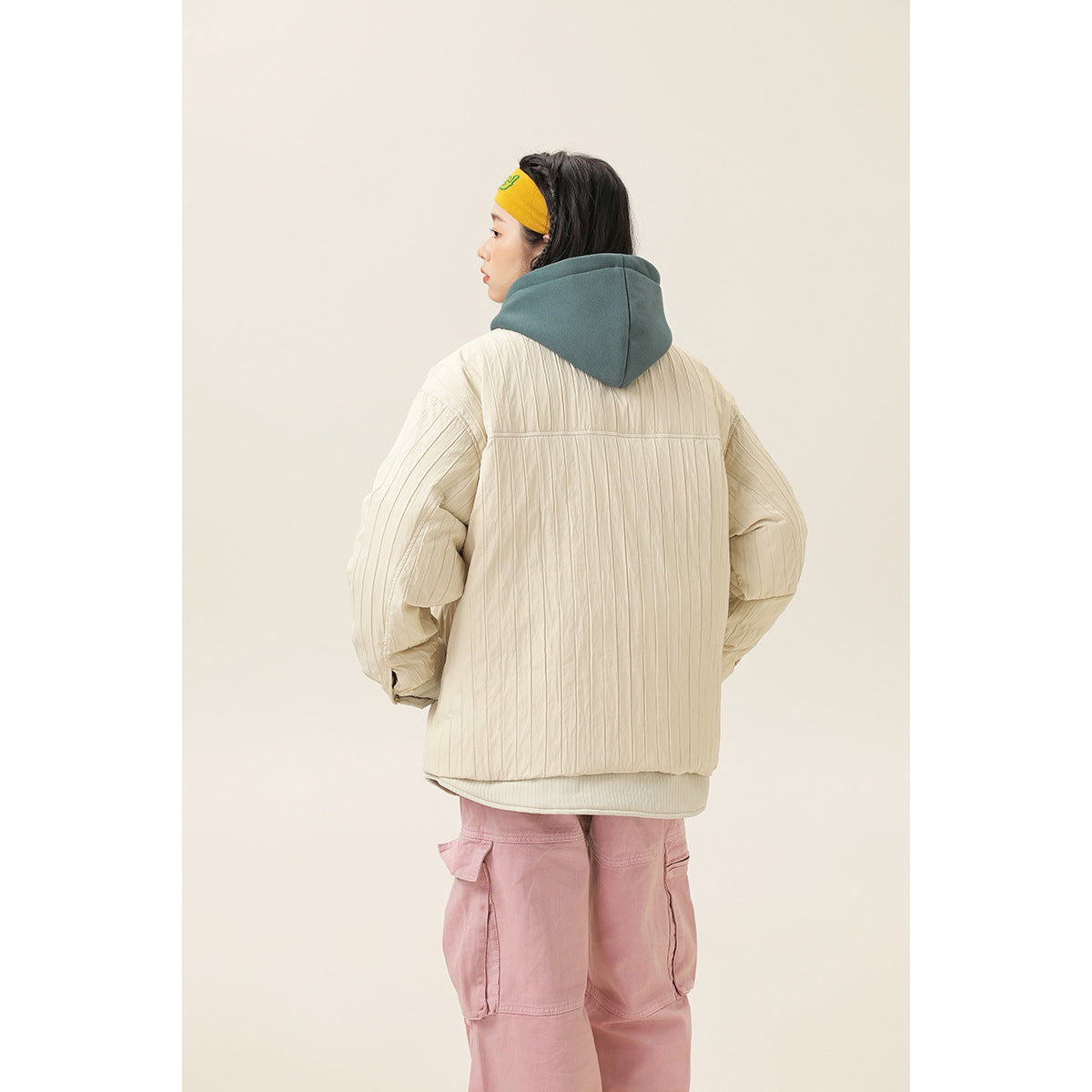 Back view of a model wearing a cream quilted jacket over a teal hooded top.