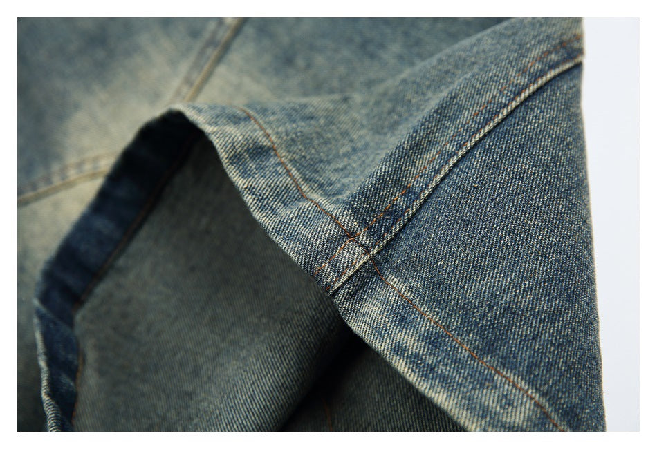 Close-up of a blue denim garment hem with folded fabric and contrasting tan stitching.