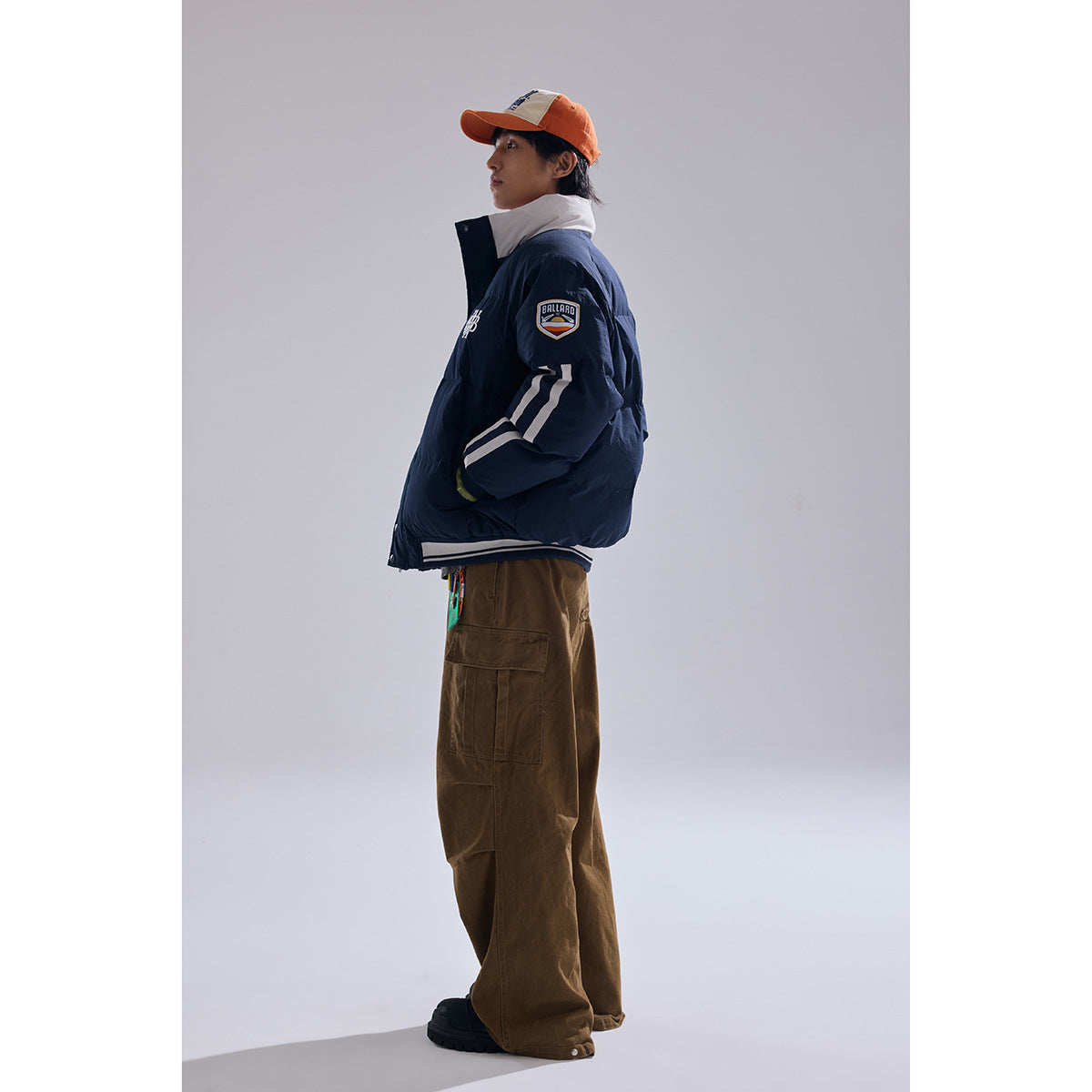 Full-length side view of a model wearing a navy padded jacket with white sleeve stripes and brown cargo pants.