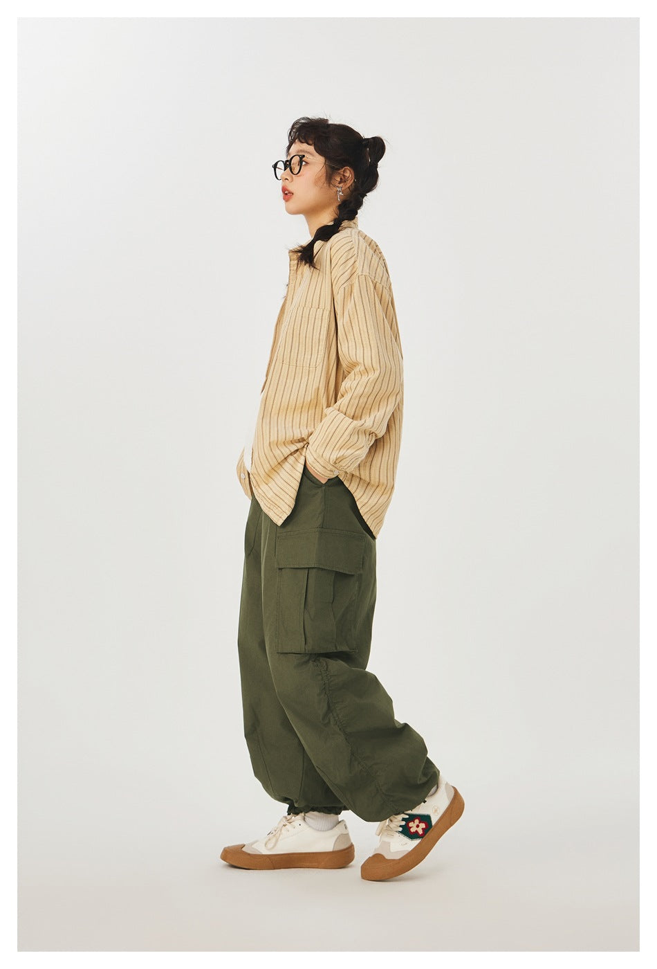 Side view of a model wearing relaxed olive cargo pants with a large flap pocket and a tan striped shirt.
