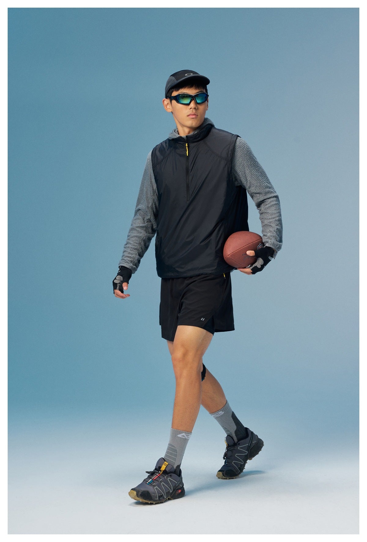 Model wearing a black sleeveless zip vest over a gray fleece top with black shorts, shown from the front.