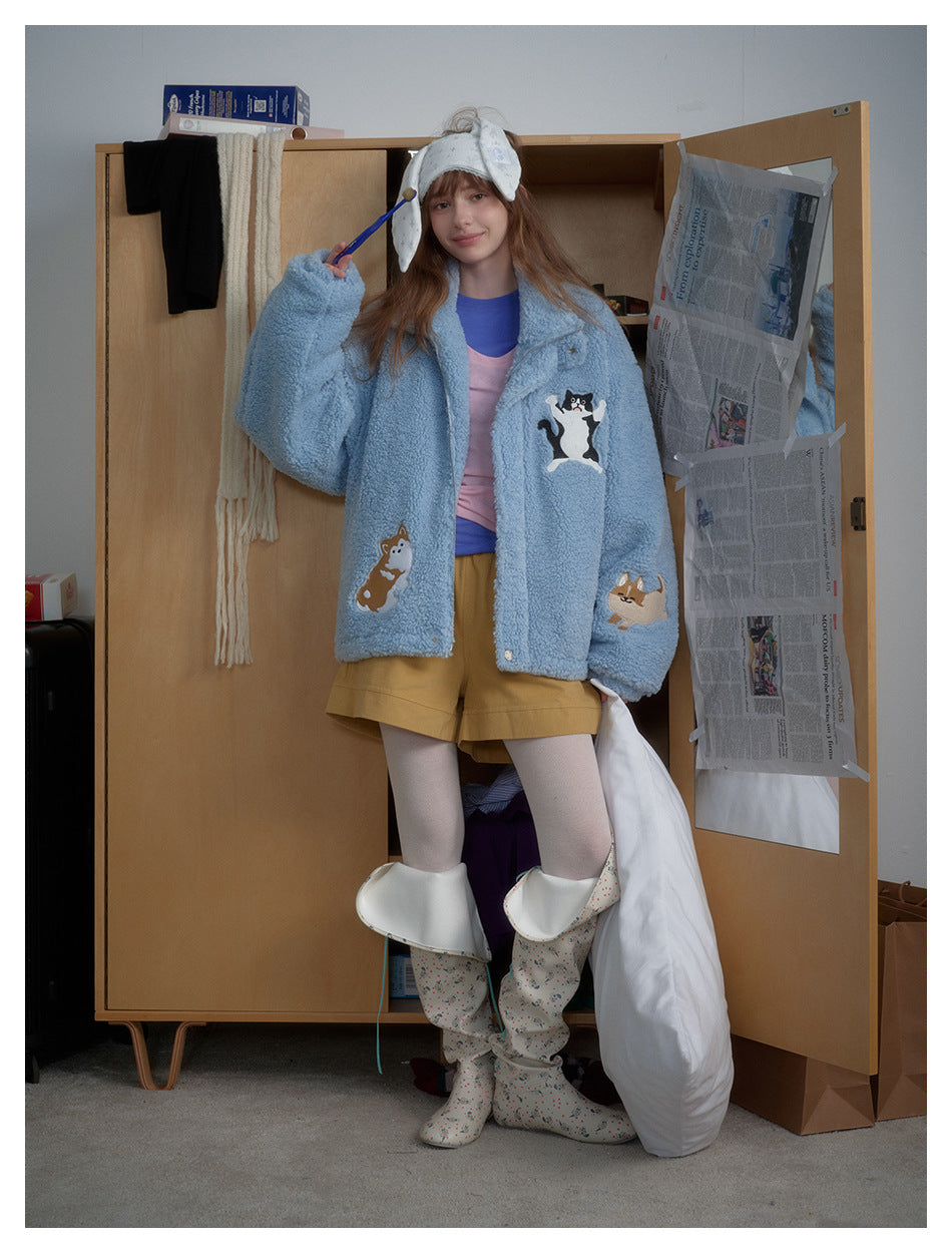 Model wearing the light blue fleece-style jacket with embroidered animals over a pink top and mustard shorts