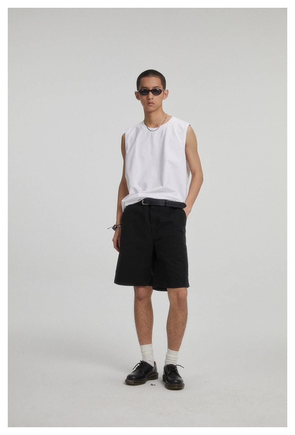 Full-length model wearing a plain white sleeveless crew-neck shirt and black shorts with a black belt.