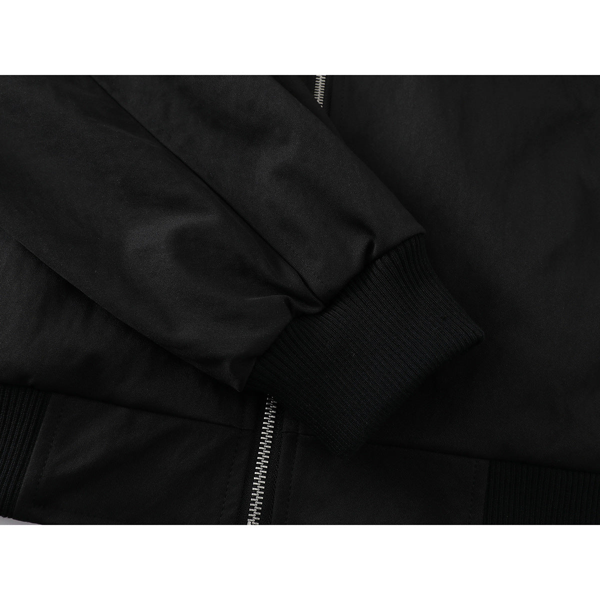 Close-up of a black jacket's sleeve and ribbed cuff, with part of the zipper and hem visible.