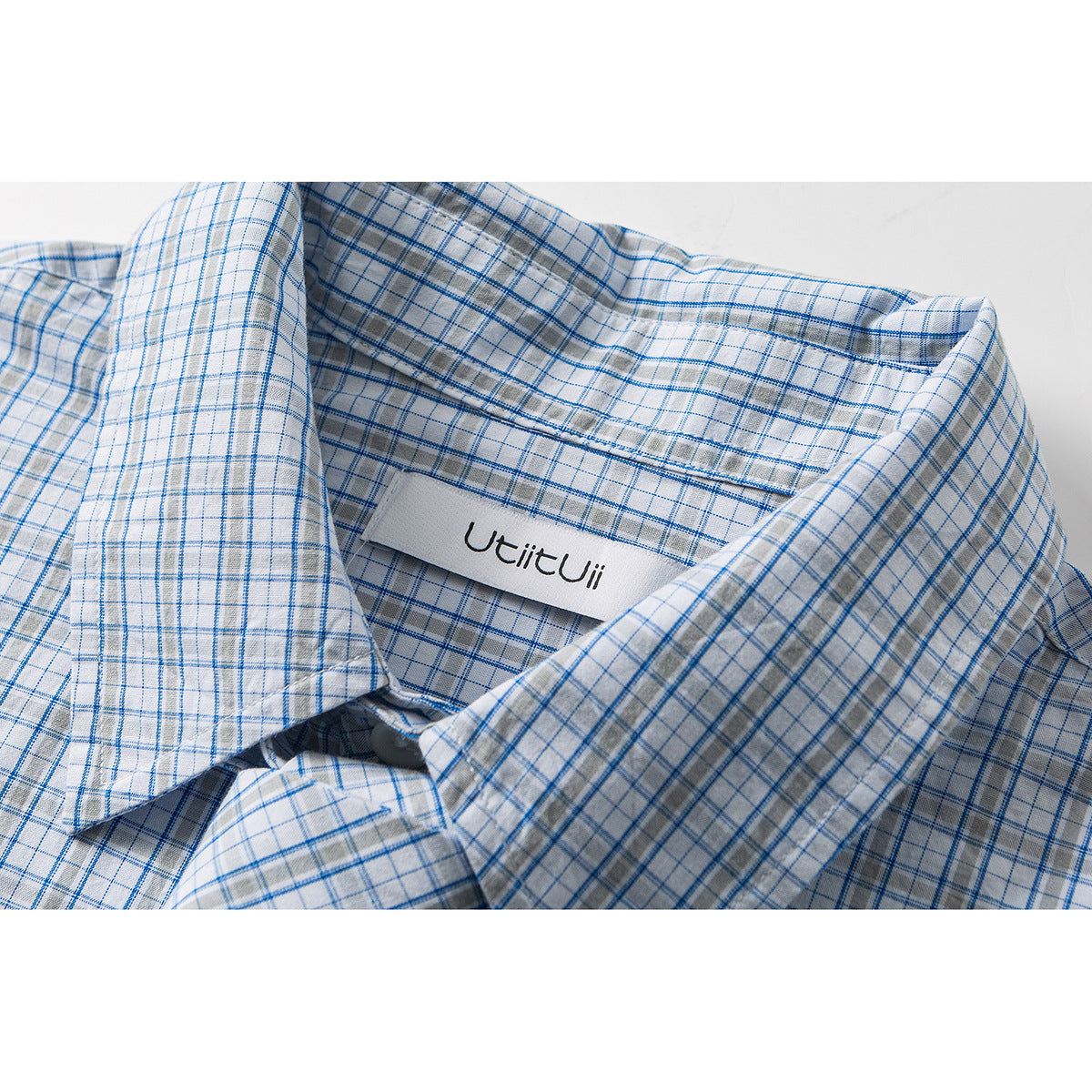 Close-up of a white shirt collar with a blue and gray windowpane check and a small sewn-in neck label.