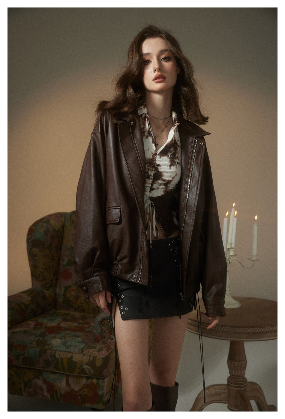Model wearing an oversized dark brown jacket, printed top, black lace-up mini skirt, and tall boots.