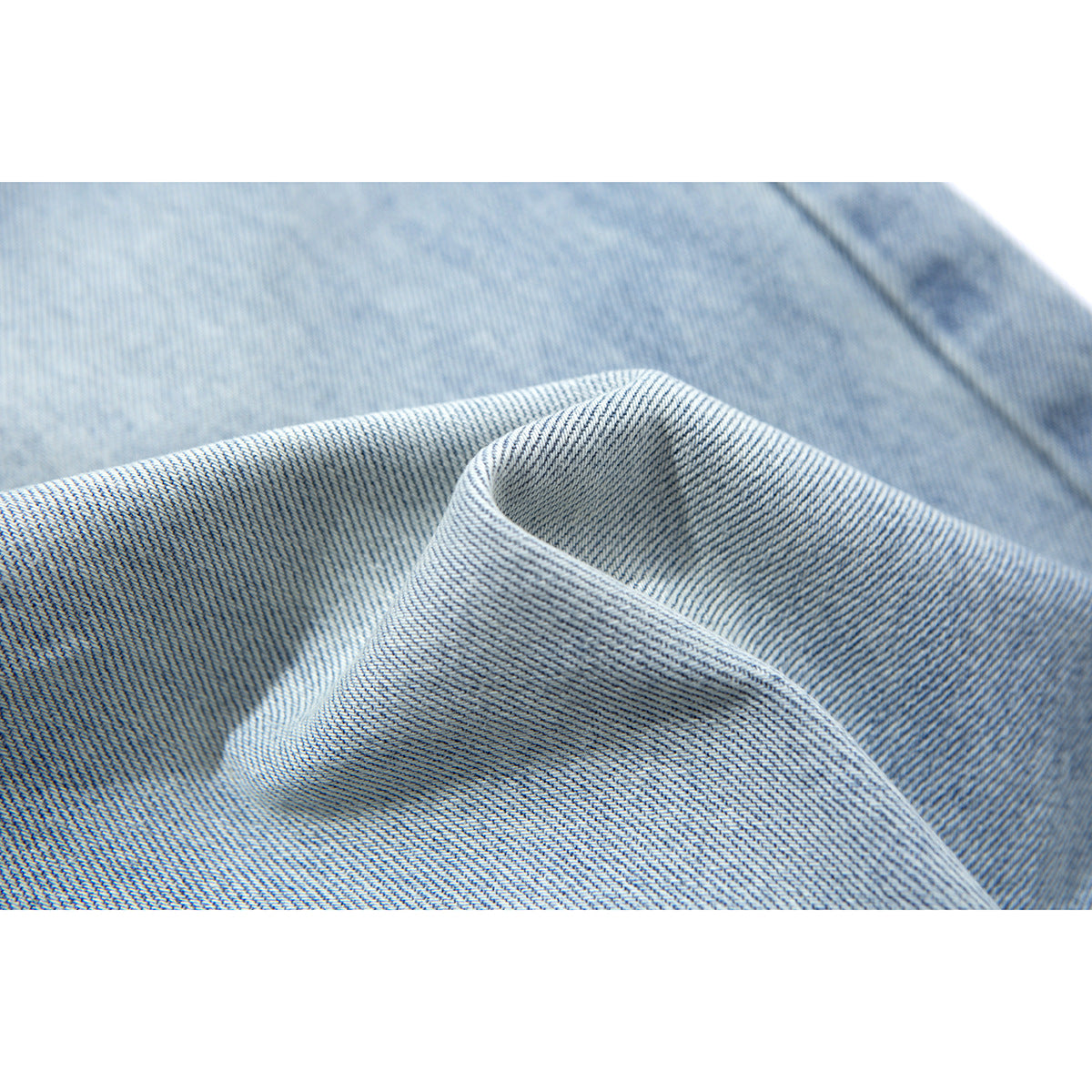 Close-up of light blue denim fabric folded to show its diagonal weave and faded coloring.