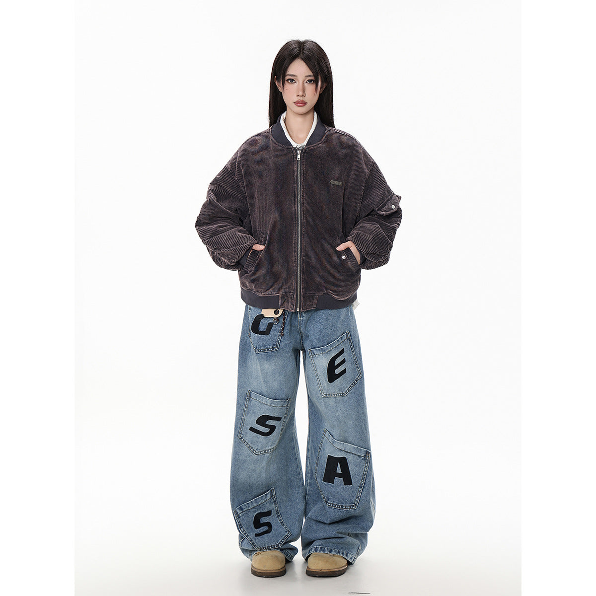 Model wearing a dark brown ribbed zip bomber jacket with oversized blue letter-patch jeans, front view.