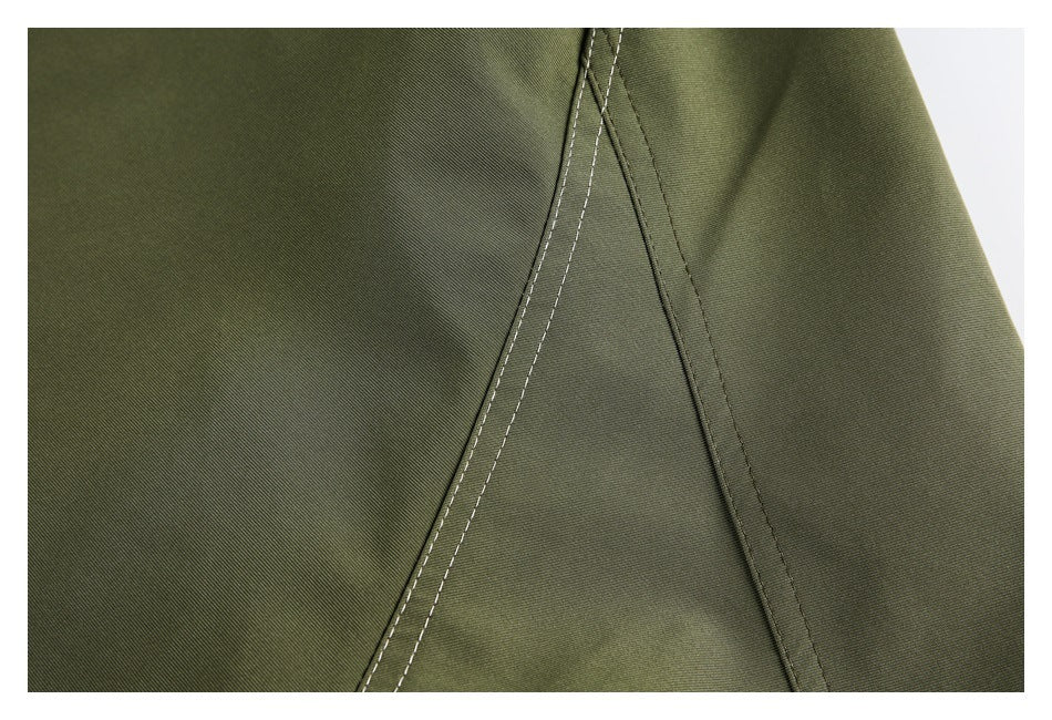 Close-up of olive-green fabric showing angled seams and light contrasting double stitching.